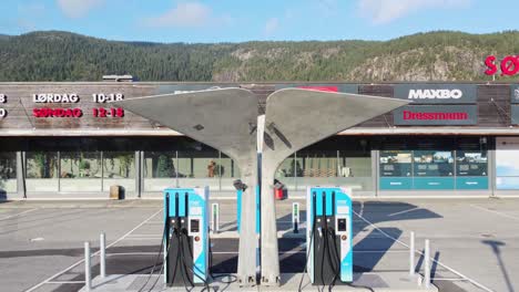 Artistic-high-speed-charger-for-electric-cars---MER-charging-station-at-Flaa-Norway---Slowly-upward-moving-aerial-with-mall-in-background