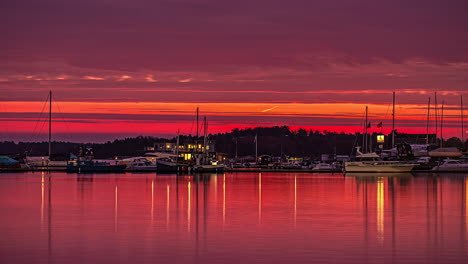 Timelapse-of-a-red-sunrise-in-a-dock-full-of-moored-boats,-with-reflections-of-calm-water