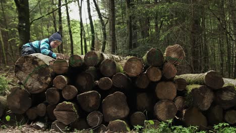 Young-boy-climbing-over-logs-in-the-forest-on-an-overcast-day