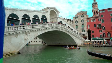 Classic-gondola-boat-sailing-the-gran-canal-under-the-famous-Rialto-bridge-crowded-with-tourist-taking-selfie