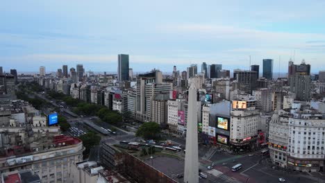 Filmische-Tiefflugaufnahme-Aus-Der-Luft,-Die-Langsam-über-Ein-Chalet-Fliegt-Und-Ein-Riesiges-Obelisk-Steinmonument-Enthüllt,-Das-In-Der-überfüllten-Stadt-Buenos-Aires,-Argentinien,-Errichtet-Wurde
