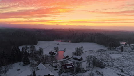 Red,-orange-and-pink-winter-sunset-landscape-aerial-view,-country-houses-with-a-lake-in-the-woodlands
