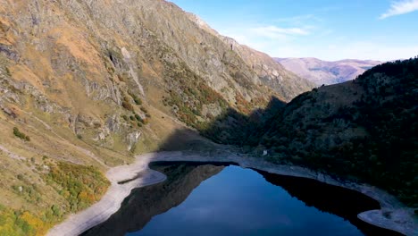 Lac-d'Oô-dam-lake-in-the-French-Pyrenees-with-low-water-level-in-the-walls,-Aerial-high-altitude-flyover-shot
