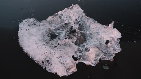 Top-down-close-up-view-of-small-piece-of-ice-on-black-sand-Diamond-Beach,-Iceland