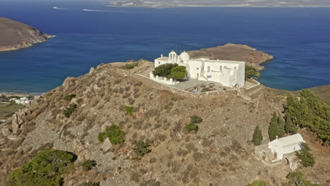 Paros-Greece-Aerial-v9-orbit-shot-drone-fly-around-monastery-of-agios-antonios-perched-atop-of-rocky-hill,-church-with-stunning-panoramic-view-of-paros-seaside-and-landscape---September-2021
