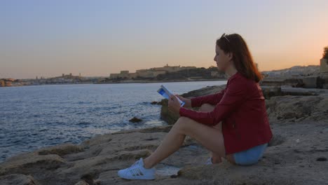 A-young-woman-sits-on-the-beach-by-the-sea-with-a-book-in-her-hands