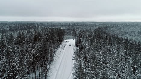 Aerial-view-of-a-car-driving-through-a-snowy-forest-in-Latvian-winter
