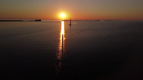 Beautiful-aerial-vibrant-high-contrast-sunset-over-calm-Baltic-sea,-rock-pier-at-Port-of-Liepaja-,-distant-sailing-boat,-wide-angle-drone-shot-moving-right