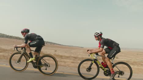slow-motion-tracking-shot-of-two-road-cycelist-professionals-riding-fast-in-the-desert's-empty-road