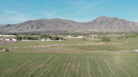 Vista-Aérea-De-Los-Campos-De-Utah-Con-Montañas-En-El-Fondo-Con-Cielo-Azul