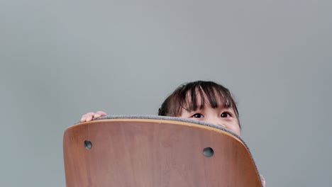 Girl-playing-to-hide-behind-wooden-armchair