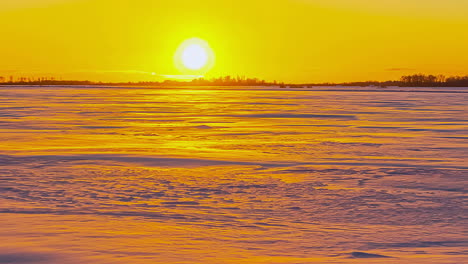 Timelapse-shot-of-sun-setting-behind-trees-over-white-frozen-field-on-the-cold-winter-evening