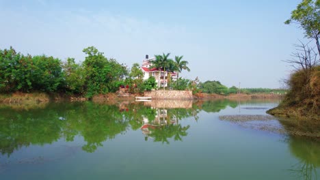 Travel-across-the-blue-green-lake-reflecting-a-luxurious-house-and-overgrown-palm-trees-and-boats-in-Vadodara,-India