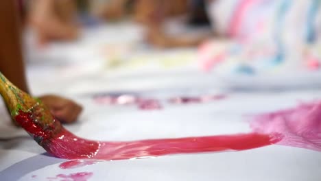Close-up-on-paintbrush-with-wet-red-paint-being-brushed-onto-large-white-sheet-of-paper-filmed-in-slow-motion