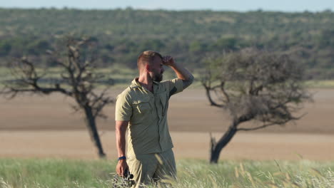 Tourist-Guy-Standing-On-Grassfield-Looking-Through-A-Telescope-Enjoying-The-Wildlife-View-In-Central-Kalahari-Game-Reserve,-Botswana,-Southern-Africa