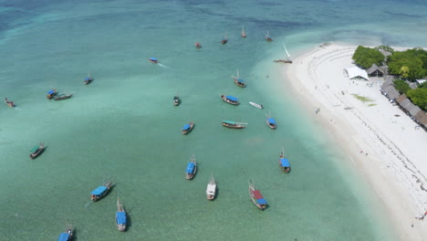 Fleet-of-fishing-boats-anchored-by-tropical-white-sand-beach,-Zanzibar