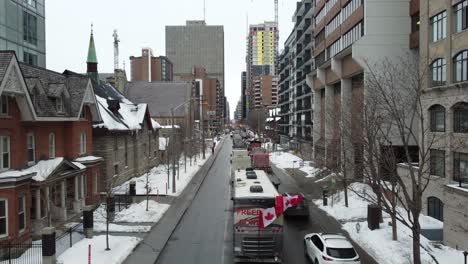 Kanadische-Flaggen-Flattern-Im-Wind-Und-Mehrere-Lastwagen-Blockieren-Eine-Straße-In-Der-Schneebedeckten-Innenstadt-Von-Ottawa,-Als-Teil-Des-Freiheitskonvois-In-Kanada