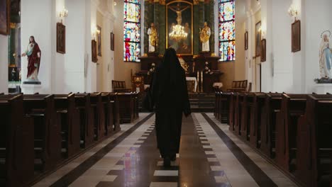 Nun-walking-inside-a-catholic-church-toward-the-sacred-altar-seen-from-behind,-religious-people-concept