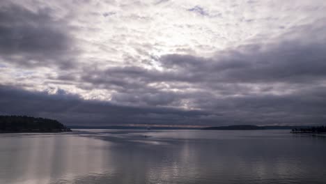 Low-dark-marine-layer-clouds-reflect-off-the-calm-still-water,-aerial-hyperlapse
