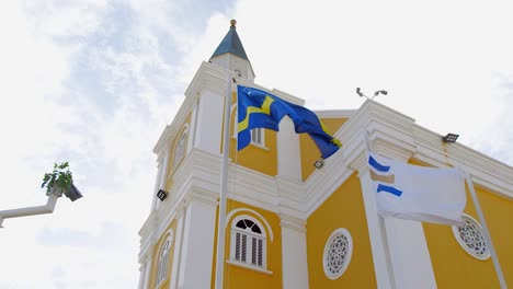 Curacao-flag-waving-in-front-of-a-beautiful-Dutch-heritage-building-in-Willemstad,-Caribbean