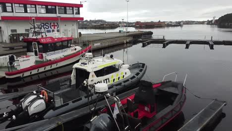 Police-boat-and-rescue-company-boat-laying-alongside-dock-in-Stavanger-Norway---Slow-forward-moving-low-altitude-aerial-in-calm-overcast-weather