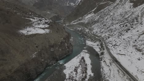 Aerial-Over-River-In-Hunza-Valley-With-Snow-Hillside-Landscape