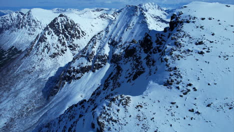 Vuelo-Lento-De-Drones-Aéreos-A-Lo-Largo-De-Enormes-Montañas-Cubiertas-De-Nieve-Iluminadas-Por-El-Sol-En-Noruega,-Europa---Hermosa-Escena-Invernal-Con-Pared-Empinada-En-El-Valle