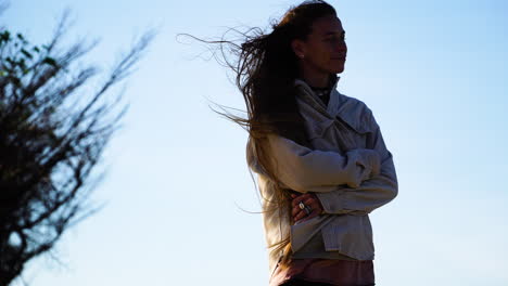 Close-up-silhouette-of-young-woman-with-long-hairs-standing-on-mountaintop-during-windy-day-in-the-evening
