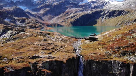Aerial-View-Of-Waterfall-Flowing-Into-Mountain-Cliff-From-Weisssee-Reservoir-Spillway-In-Austria