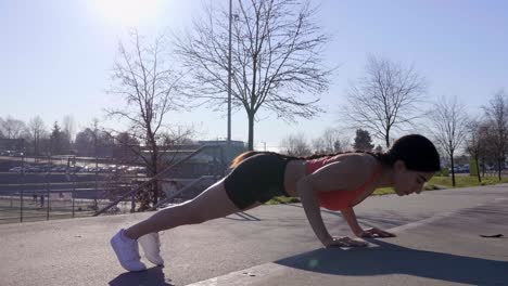 Athletic-young-woman-doing-pushups-on-curb-with-bright-sun-behind