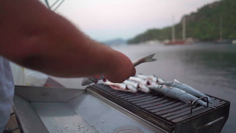 Small-whole-gutted-fish-are-placed-onto-outdoor-grill-on-moored-yacht
