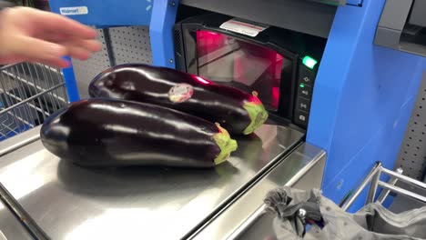 Placing-egg-plants-on-self-checkout-scanner-to-weigh-fruits-and-vegetables-in-big-box-superstore-grocery-market-as-the-future-of-cashiers-replacements
