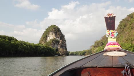 Zeitlupe-Eines-Hölzernen-Thailändischen-Longtail-Bootes,-Das-Mit-Bunten-Blumen-Geschmückt-Ist-Und-Bei-Sonnenuntergang-Den-Fluss-Hinunter-Schwimmt,-Mit-Kalksteinbergen-Und-Mangrovenwäldern-In-Der-Stadt-Krabi-In-Thailand