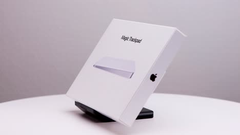 Drehung-Der-Weißen-Verpackung-Des-Mac-Magic-Trackpads-Gegen-Den-Uhrzeigersinn-Auf-Dem-Ausstellungsständer-Mit-Sichtbarem-Apple-Firmenlogo-An-Der-Seite