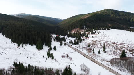 Aerial-flyover-above-road-running-through-scenic-winter-valley-in-Romania