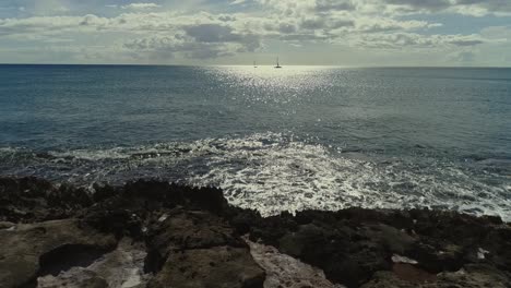 Ascending-view-rocky-pacific-ocean-shore,-Sailing-boats-silhouette-horizon,-Hawaii