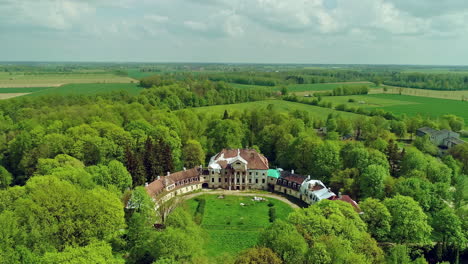 Aerial-backwards-shot-showing-idyllic-landscape-surrounding-old-castle-building-in-summer---Latvia,Europe