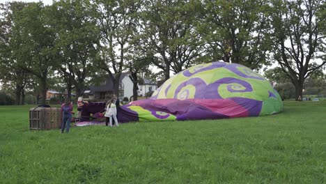 Colorful-hot-air-balloon-on-ground-being-heated-with-crew-working-nearby,-handheld-view