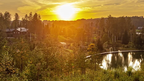 Golden-sunset-behind-forest-trees-in-idyllic-scenery-with-lake-and-holiday-apartments---time-lapse