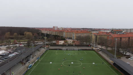 Aerial-tilt-down-ascending-over-people-training-on-soccer-field-at-Malmo-Stadium,-Sweden