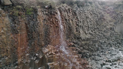 Luftparallaxe-Um-Einen-Kleinen-Wasserfall,-Der-Die-Basaltklippe-Studlagil-Canyon,-Island,-Hinunterfließt