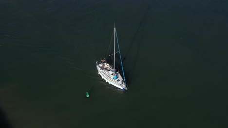 Sailing-yacht-with-long-shadow-navigates-on-her-motor-along-the-green-buoy-over-the-clear-green-waters-of-the-Mediterranean