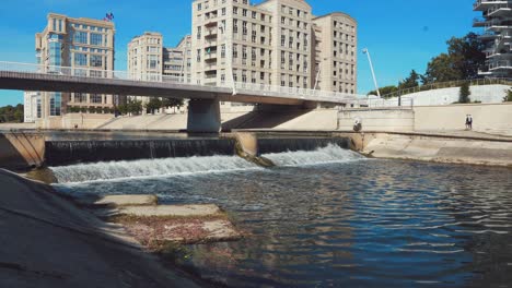 move-towards-the-small-waterfall-under-the-bridge-in-the-city,-Montpellier---France