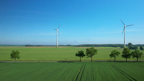 Backwards-aerial-movement-of-wind-turbines-in-countryside,-road,-trees-and-car-passing