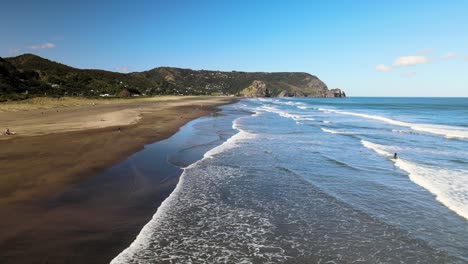 Panning-across-Piha-black-sand-beach-with-reflection-of-surfer-walking-out-of-the-ocean-water