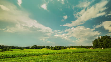 Static-shot-of-mystic-white-clouds-flying-over-green-field-with-hay-bales-in-timelapse-at-daytime