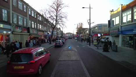 Looking-Down-The-Broadway-A4020-In-Southall-With-Traffic-Going-Past-And-People-Shopping-In-Late-Afternoon-On-16-January-2022