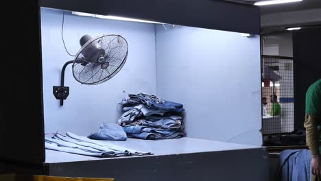 Caja-De-Secado-Con-Ventilador-Girando-Con-Jeans-Colocados-Planos-En-Fábrica-En-Karachi,-Pakistán