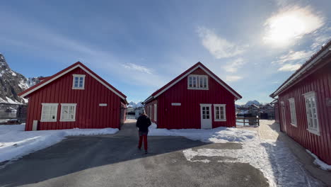 Young-male-tourist-walking-towards-Traditional-Norwegian-Fisherman-Cabins-on-a-sunny-day,-exploring-the-view