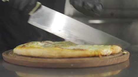 Close-up-view-of-chef-cutting-freshly-made-pizza-into-slices-with-kitchen-knife